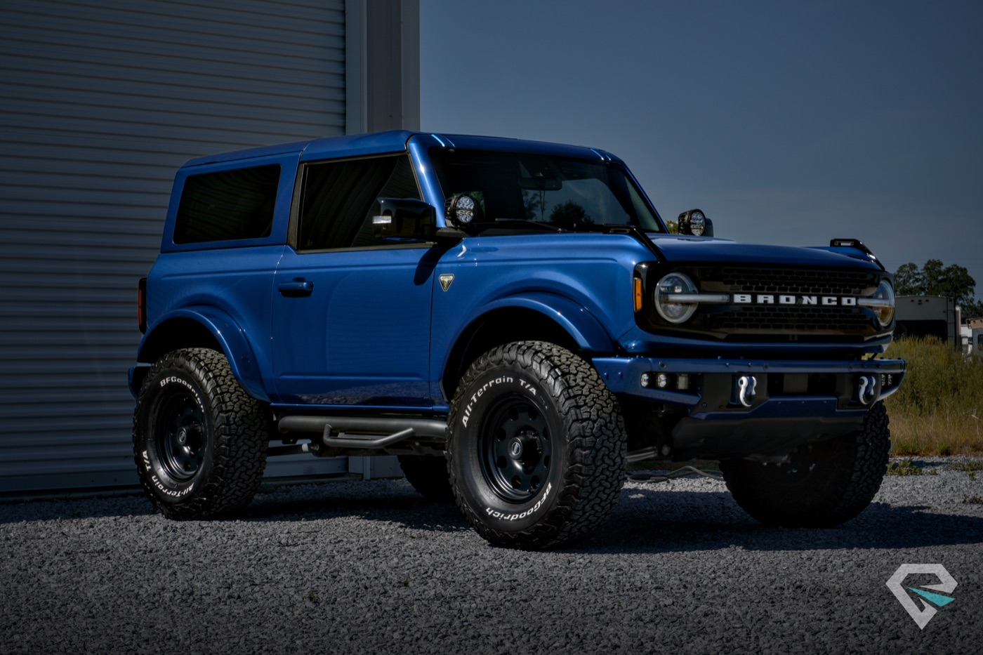 Blue Ford Bronco two-door on gravel in front of the shop